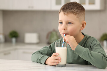 Cute boy drinking fresh milk from glass at white table in kitchen, space for text