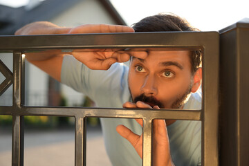 Concept of private life. Curious man spying on neighbours over fence outdoors