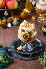 Obraz na płótnie Canvas Dessert, portioned apple trifle with oat crumble, spiced cake, custard and whipped cream in a glass glass in a Christmas style.
