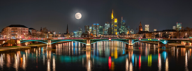 Der Vollmond mit der abendlichen, künstlich beleuchteten Skyline von Frankfurt am Main im Panoramaformat