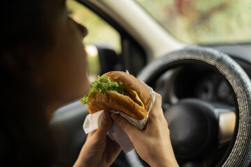 Woman eating hamburger in car in morning traffic jam on the way to work