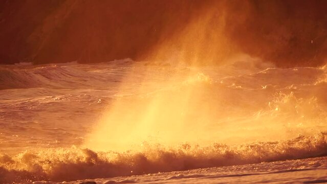 Storm Wave Sunset. Storm wave approaching the coast at golden burning sunset with spray originated by wind in backlight. Seascape with large breaking waves. Weather and climate change