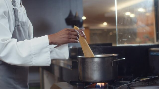 Cropped shot of cook adding spaghetti to boiling water while cooking pasta at open kitchen at hotel restaurant