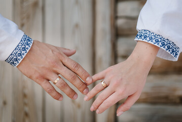 Rings and engagement. Bride and groom wearing embroidered dress and shirts hold hands together...