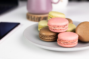 Vibrant macarons arranged on a plate, resting delicately on a pristine white desk. Perfect for bakery banners and kitchen decor.