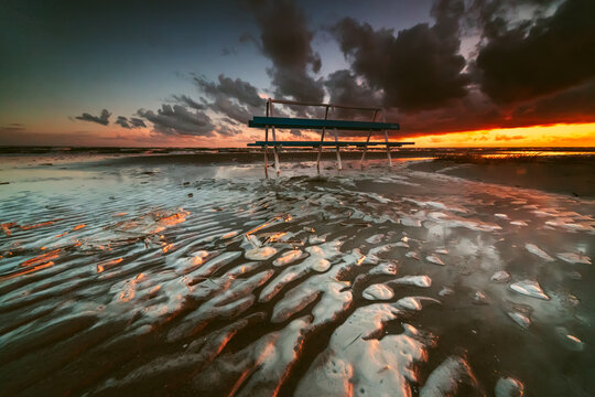 Silhouette of a bench on a flooded beach after a storm at sunset, Parnu, Estonia