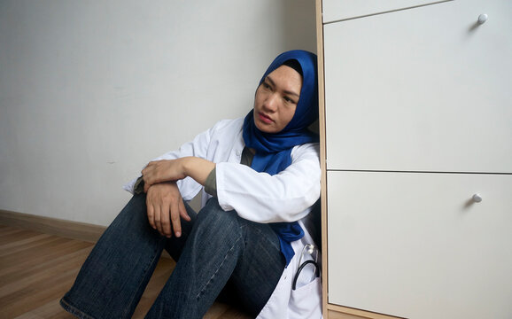 Young female Muslim doctor sitting on floor with tired and sad expression