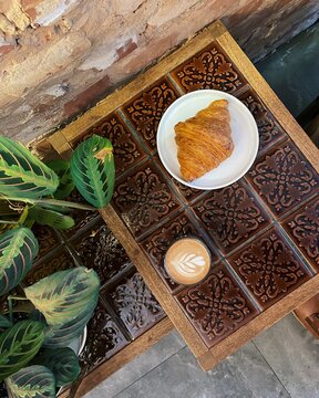 Overhead view of a moccachino and croissant on a table in a rustic setting