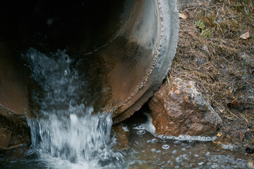 The river is polluted by industrial waste from a drainpipe that dumps sewage into the water, harming the natural ecosystem.