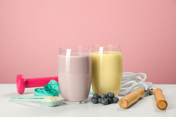 Tasty shakes with blueberries, sports equipment, measuring tape and powder on white table against...