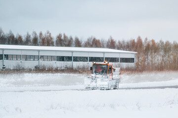 An orange truck with a salt and sand spreader clears the snow and ice from the road. The winter service vehicle works to make the public roads safe and prevent corrosion.