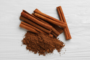 Dry aromatic cinnamon sticks and powder on white wooden table, top view