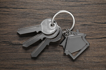 Keys with keychain in shape of house on wooden table, top view