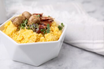 Cooked cornmeal with bacon, mushrooms and microgreens in bowl on white marble table, closeup. Space...