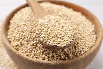 Dry quinoa seeds and spoon in bowl on white table, closeup