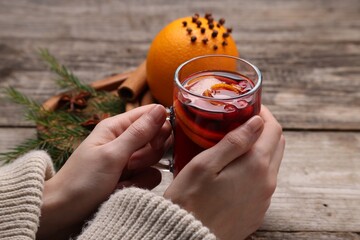 Woman with glass cup of aromatic mulled wine at wooden table, closeup