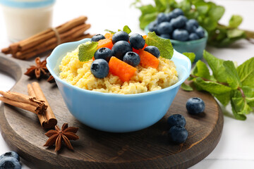 Tasty millet porridge with blueberries, pumpkin and mint in bowl on white table, closeup - obrazy, fototapety, plakaty
