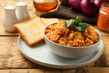 Delicious red lentils with parsley in bowl served on wooden table, closeup