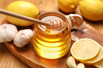 Jar with honey, garlic, lemons and dipper on table, closeup
