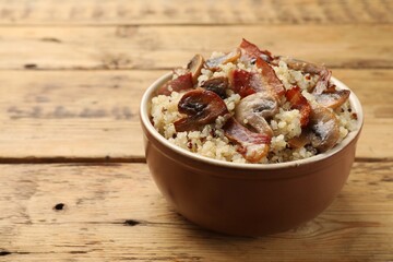 Tasty quinoa porridge with fried bacon and mushrooms in bowl on wooden table, closeup. Space for text
