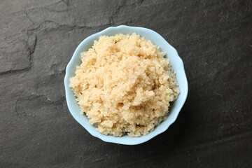 Tasty quinoa porridge in bowl on black textured table, top view