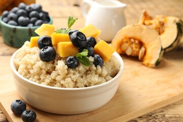 Tasty quinoa porridge with blueberries, pumpkin and mint in bowl on wooden table, closeup