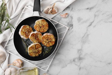 Frying pan with fried garlic, rosemary and oil on light marble table, flat lay. Space for text