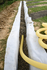 Yellow corrugated pipe with perforation in a trench with crushed stone and geotextile. Drainage...