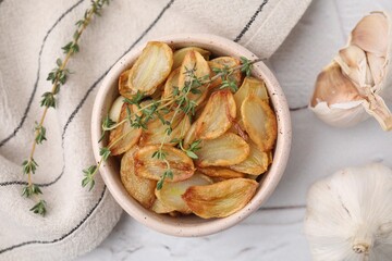 Fried garlic cloves with thyme in bowl on white table, flat lay