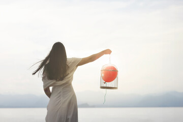 surreal woman goes to free her red balloon held prisoner in cage, concept of growth becoming adults