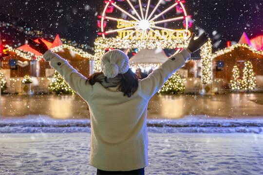 A happy tourist woman stands in front of the illuminated Christmas market of Bergen, Norway, with snow