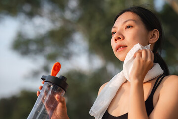 Young Asian woman takes a relaxing walk, wiping off sweat after jogging in the park.