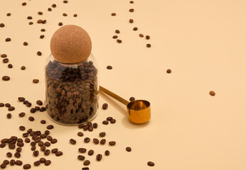 Coffee brown beans in a glass jar and scattered on a table. A gold coffee spoon. Copy space for...