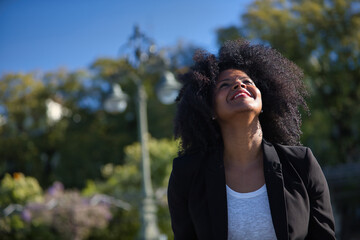 Portrait of young, beautiful, black woman with afro hair, wearing jacket, looking at the sky,...