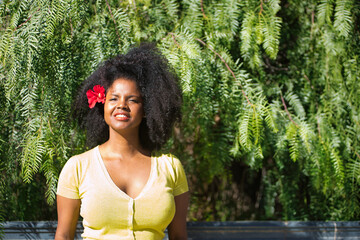 Portrait of young, beautiful, black woman with afro hair, with yellow t-shirt and a red flower in...