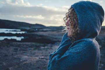 Fototapeta premium One woman hugging herself with love and care and smile looking enjoying scenic destination travel place. Sky in background, Hood on head. Concept of freedom and traveler lifestyle people female