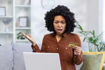 Problems with the financial account. Young upset African American woman sitting on sofa at home...