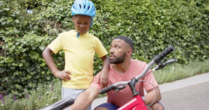 Happy african american father teaching son about bicycle in garden, slow motion