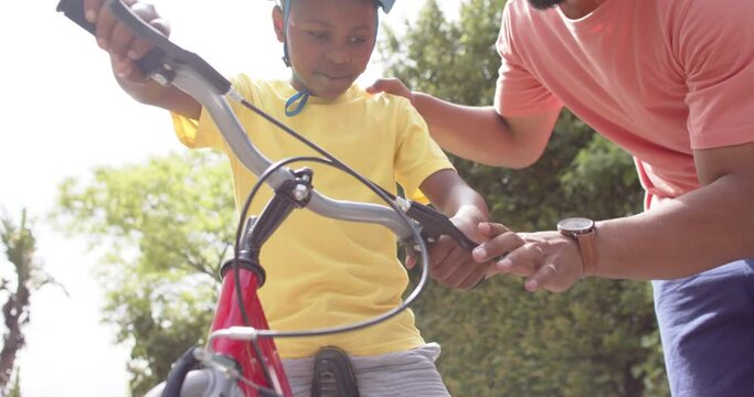 African american father teaching son to ride bicycle in sunny garden, slow motion