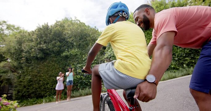 African american father teaching son to ride bicycle, mother and sister clapping, slow motion