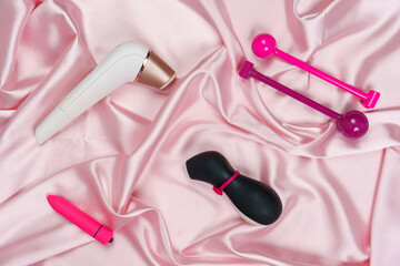 Sex toys: Clitoral Stimulator Satisfyer, vibration bullet, lubricant, kegel vagina laser device isolated on a pink silk sheet. Sex shop. Female health.