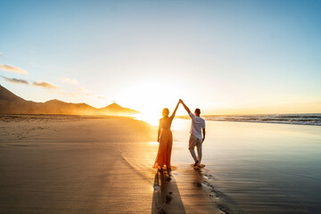 Vacation lovely couple walking on amazing beach together, in love, holding hands. Back view. Sunset...