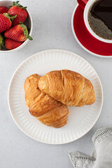 A fresh croissant with fresh strawberries and coffee. Croissant with black coffee.