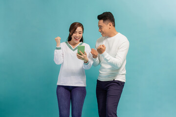 Cheerful attractive couple standing isolated over blue, using mobile phone, celebrating success - 692459049