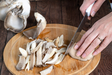 A woman slices an oyster mushroom on a cutting board. Cooking fresh wild mushrooms. - obrazy, fototapety, plakaty