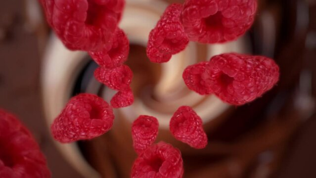 Raspberries spiraling and falling in the liquid milk chocolate slow motion