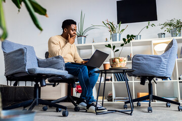 Young black men sitting in coworking space working while using laptop.