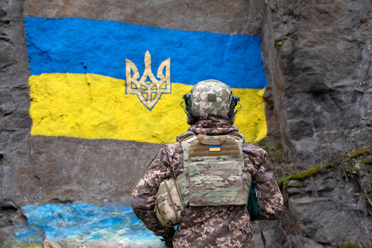 Ukrainian soldier looking at ukrainian flag painted on garnite wall
