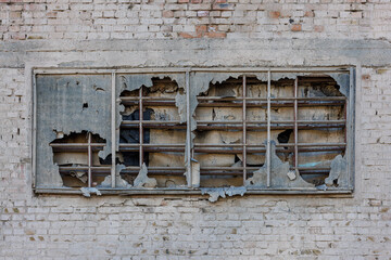 old window covered with torn ruberoid material and old wooden planks on white brick wall of an...
