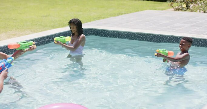 Happy african american parents and daughter playing with water pistols in sunny pool, slow motion